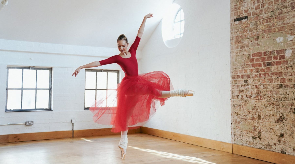 Ballet dancer in a red dress dancing en pointe in a light-filled studio