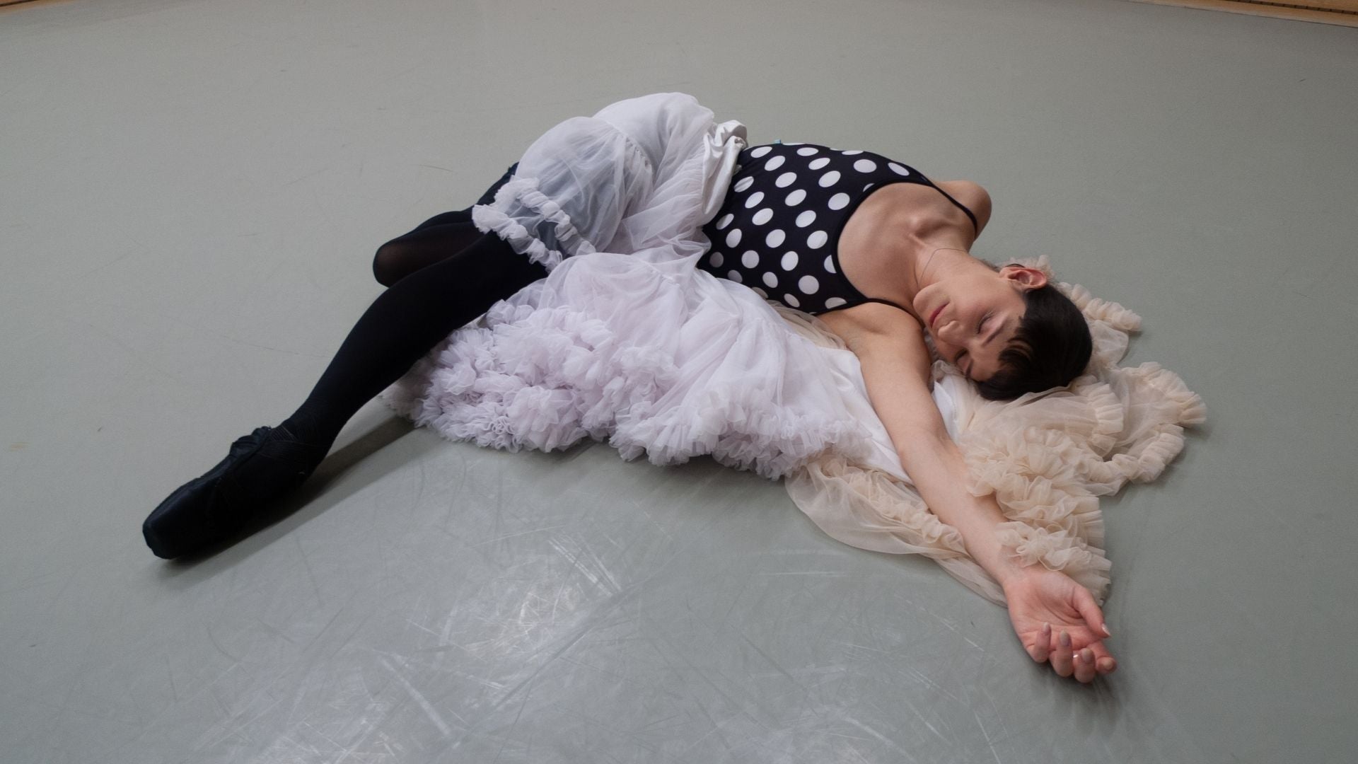 ballet dancer wearing Imperfect Pointes polka dot camisole leotard lying down on the studio floor posing on top of a pile of fluffy skirts
