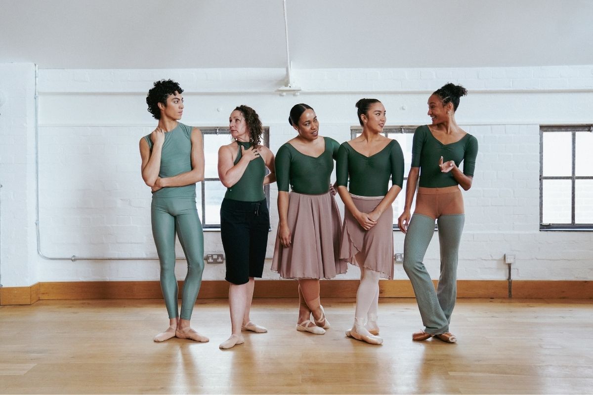 a male dancer and four female dancers in a row having a conversation dressed in green ballet wear