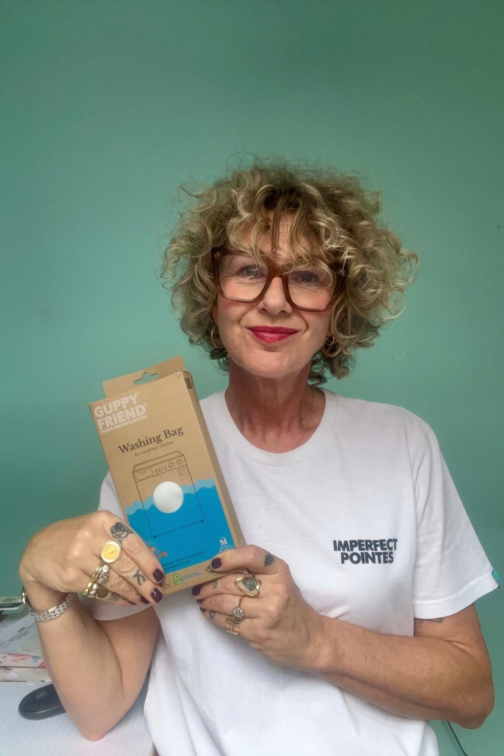 Imperfect Pointes founder Helen Banks holding a GUPPYFRIEND washing bag box, wearing an Imperfect Pointes T-shirt.