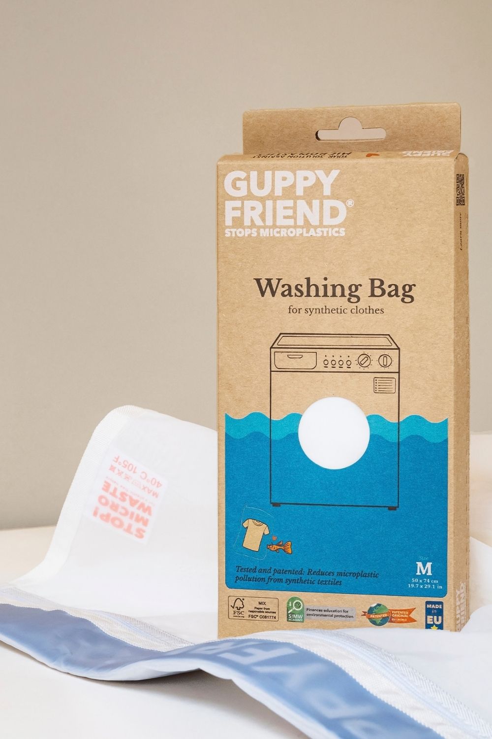 White GUPPYFRIEND washing bag with blue trim beside its cardboard packaging.stop micro plastics