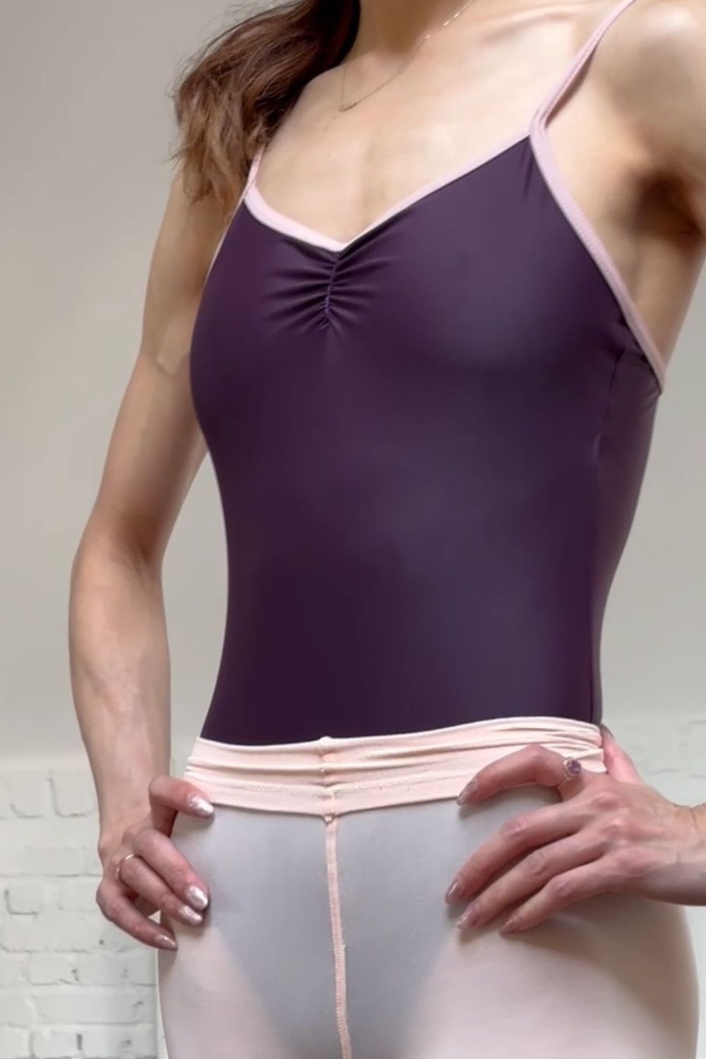 A woman wearing a cherry noir camisole leotard with oyster straps and a pinch front.