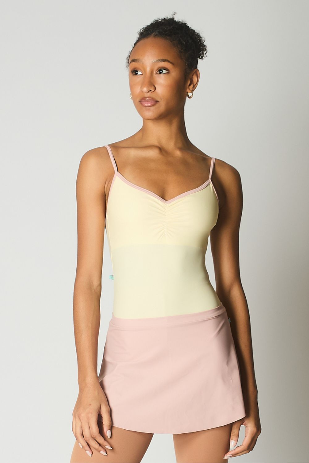 Ballet dancer wearing a light yellow ballet leotard stylecamisole and pink skirt against a plain background
