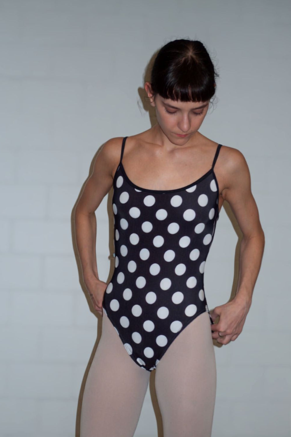 A professional ballerina wearing the Cali Camisole ballet leotard in black with white polka dots – front view, with pink tights
