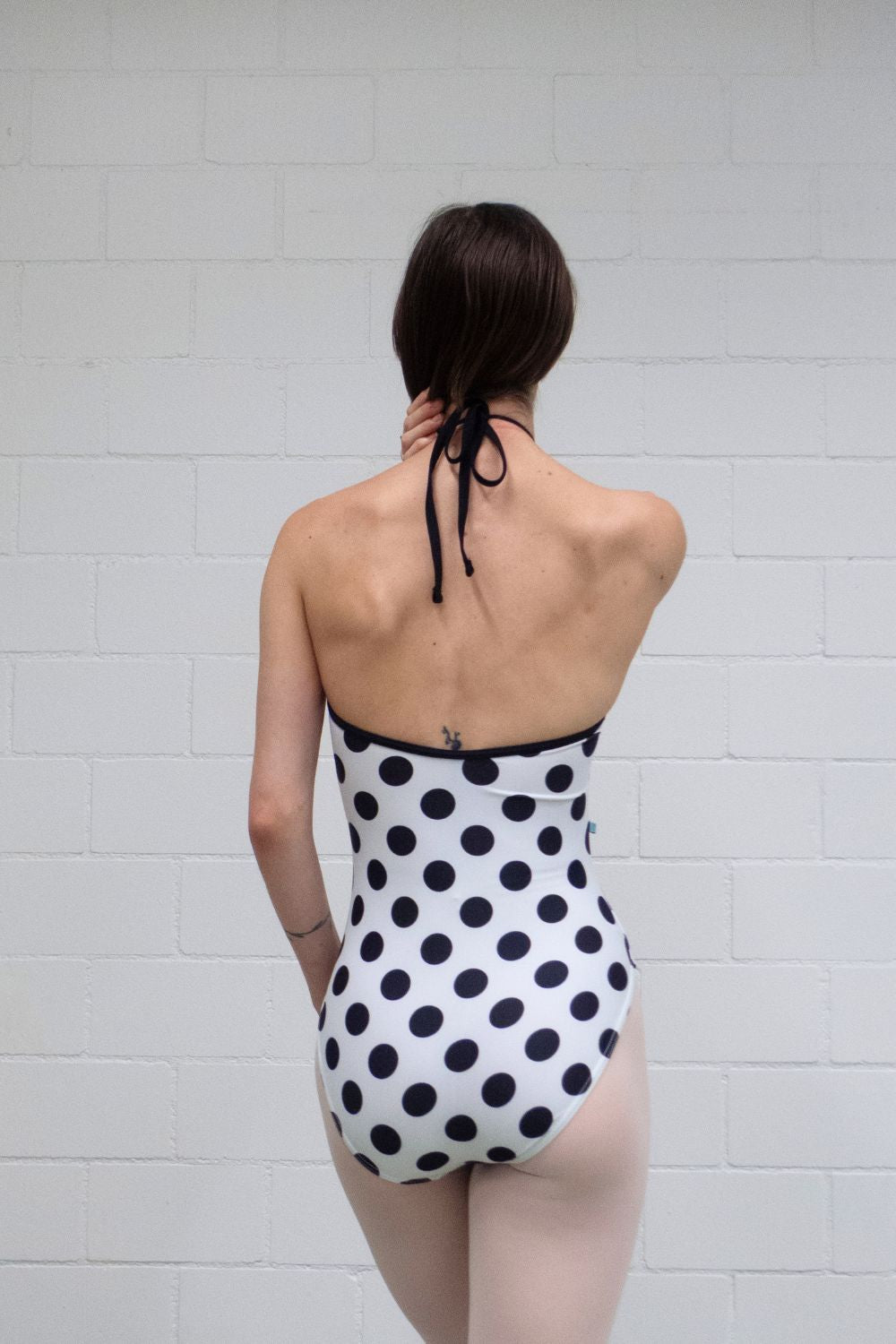 A professional ballet dancer wearing the Imperfect Pointes Eastbourne tie-neck leotard – back view showing the open back and black polka dot print