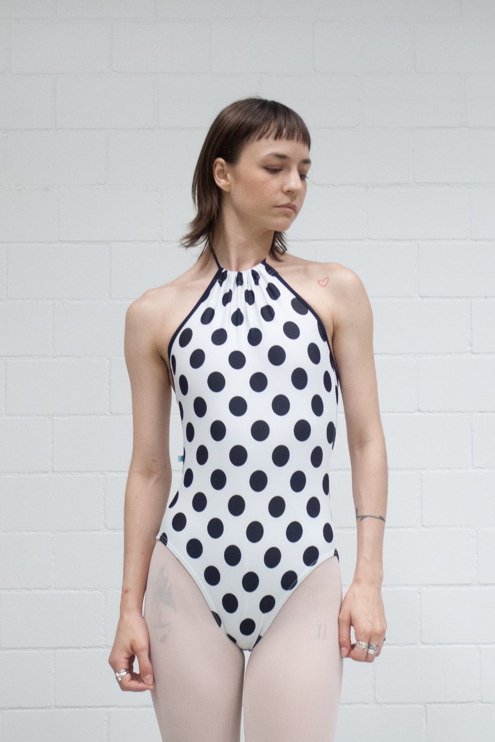 A professional ballet dancer wearing Imperfect Pointes new Eastbourne halter neck leotard with pink tights, facing front against a white wall