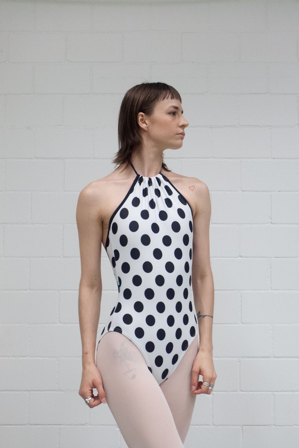 A professional ballet dancer wearing the Imperfect Pointes Eastbourne tie-neck ballet leotard in white with black polka dots – second front view